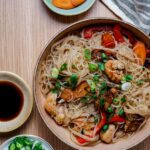 a bowl of glass noodles and vegetables with condiments on the side
