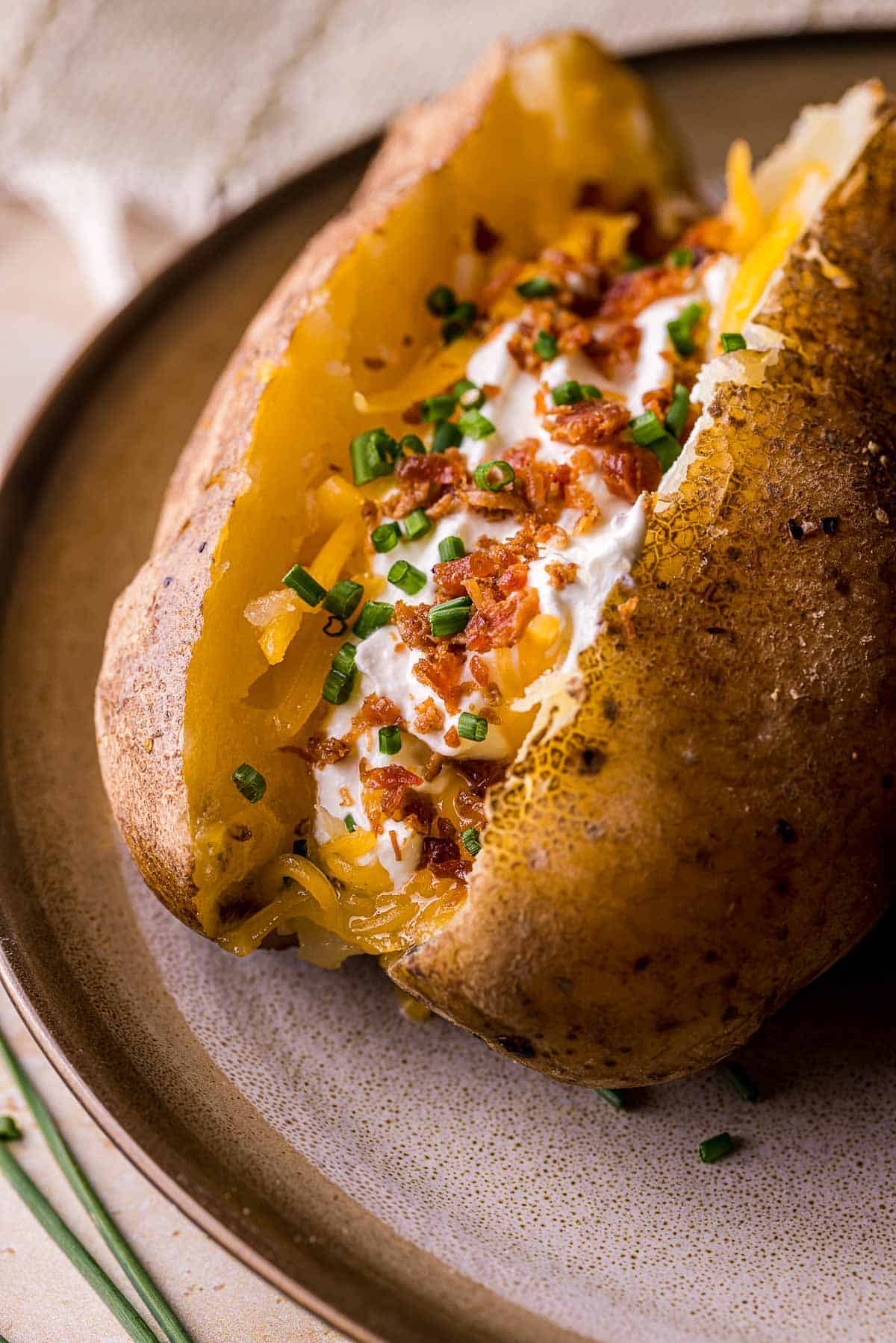 close up of baked potato topped with cheese, sour cream, bacon and chives