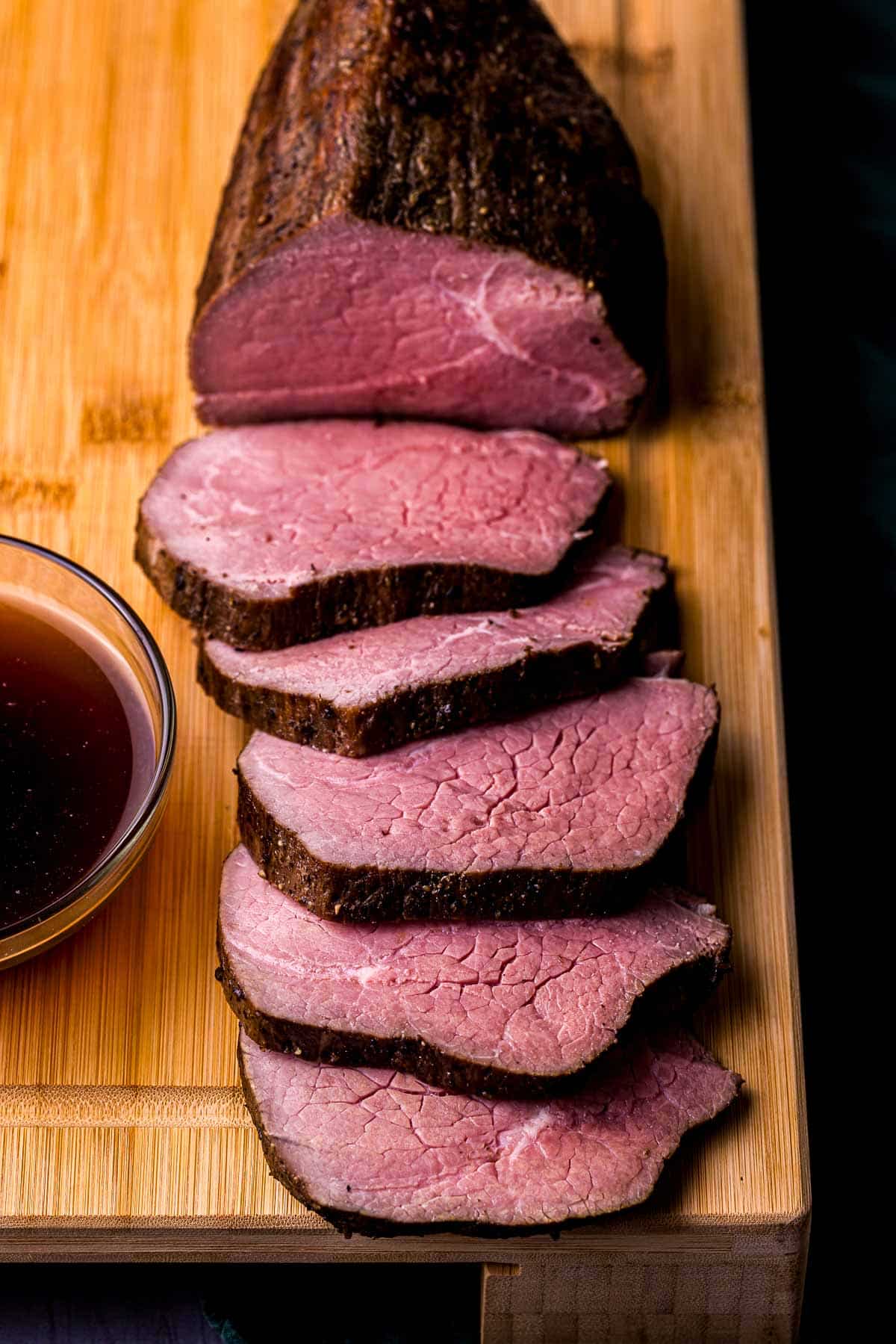 slices of beef on a wood board with jus ont he side
