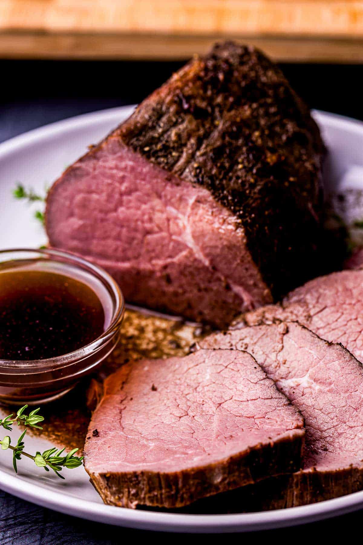 pieces of roast beef on a plate drizzle with liquid and bowl of brown jus on the side