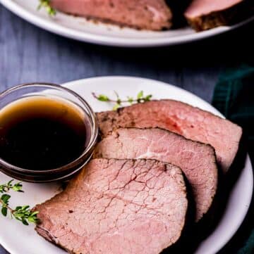 a plate of sliced roast beef with fresh thyme and a bowl of brown liquid