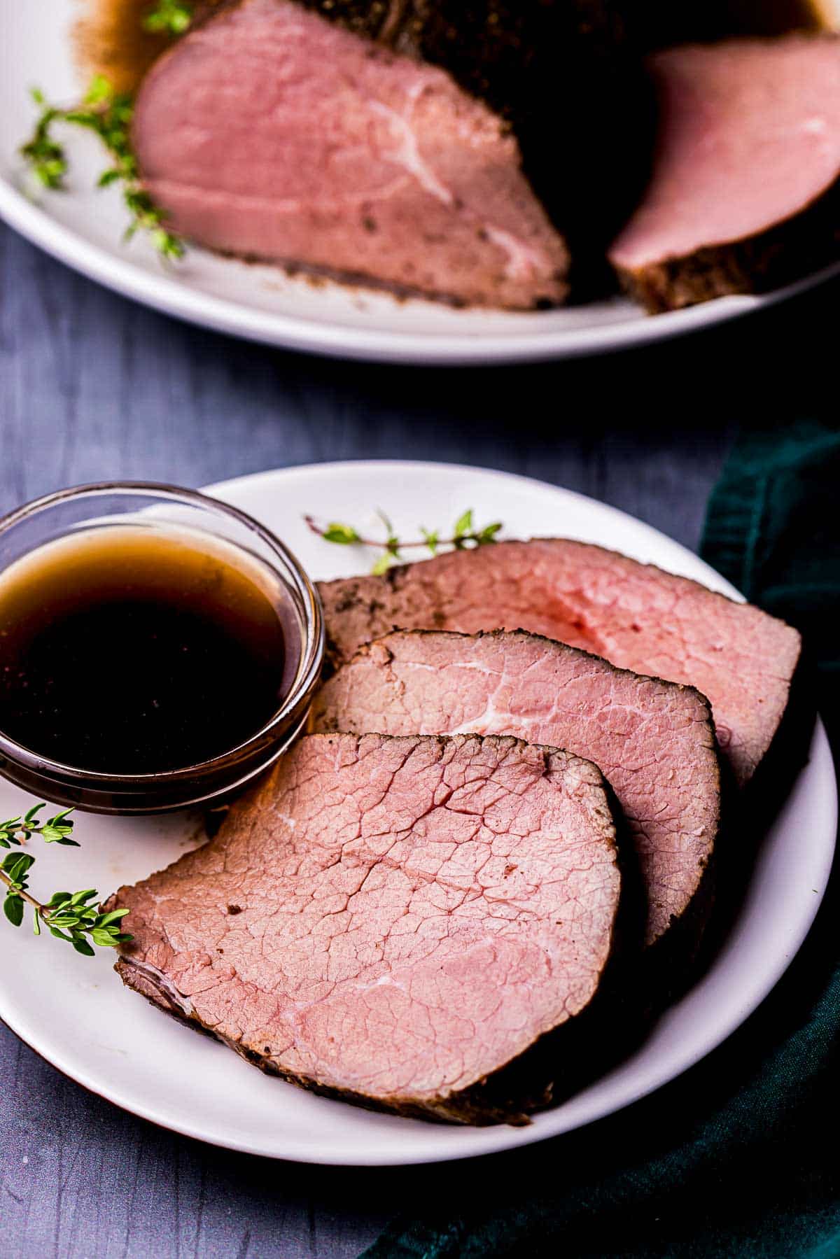 a plate of sliced roast beef with fresh thyme and a bowl of brown liquid