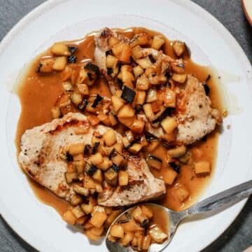 2 pork chops on a plate with apple brandy sauce (orange colored)