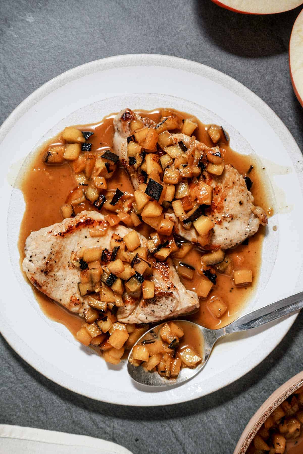 2 pork chops on a plate with apple brandy sauce (orange colored)
