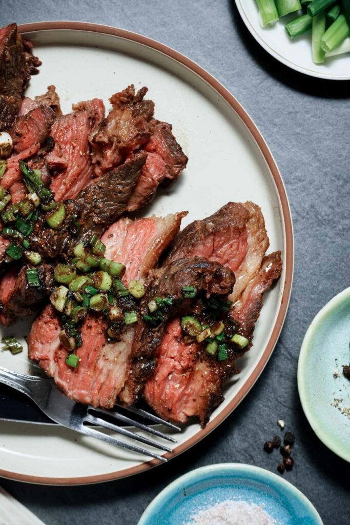 rare sliced meat on a white plate with greens on top