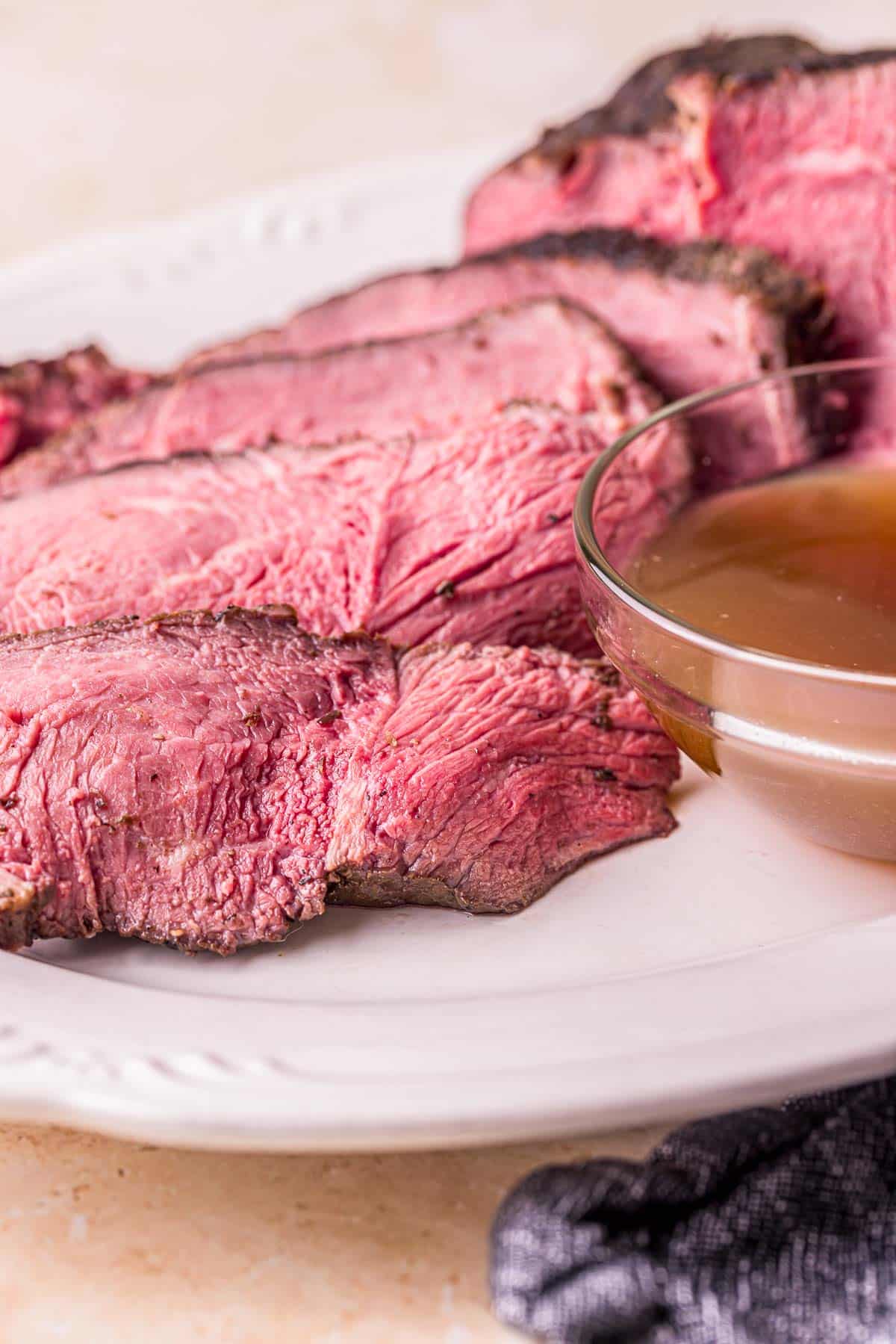 sliced of rare beef on a plate with jus on the side