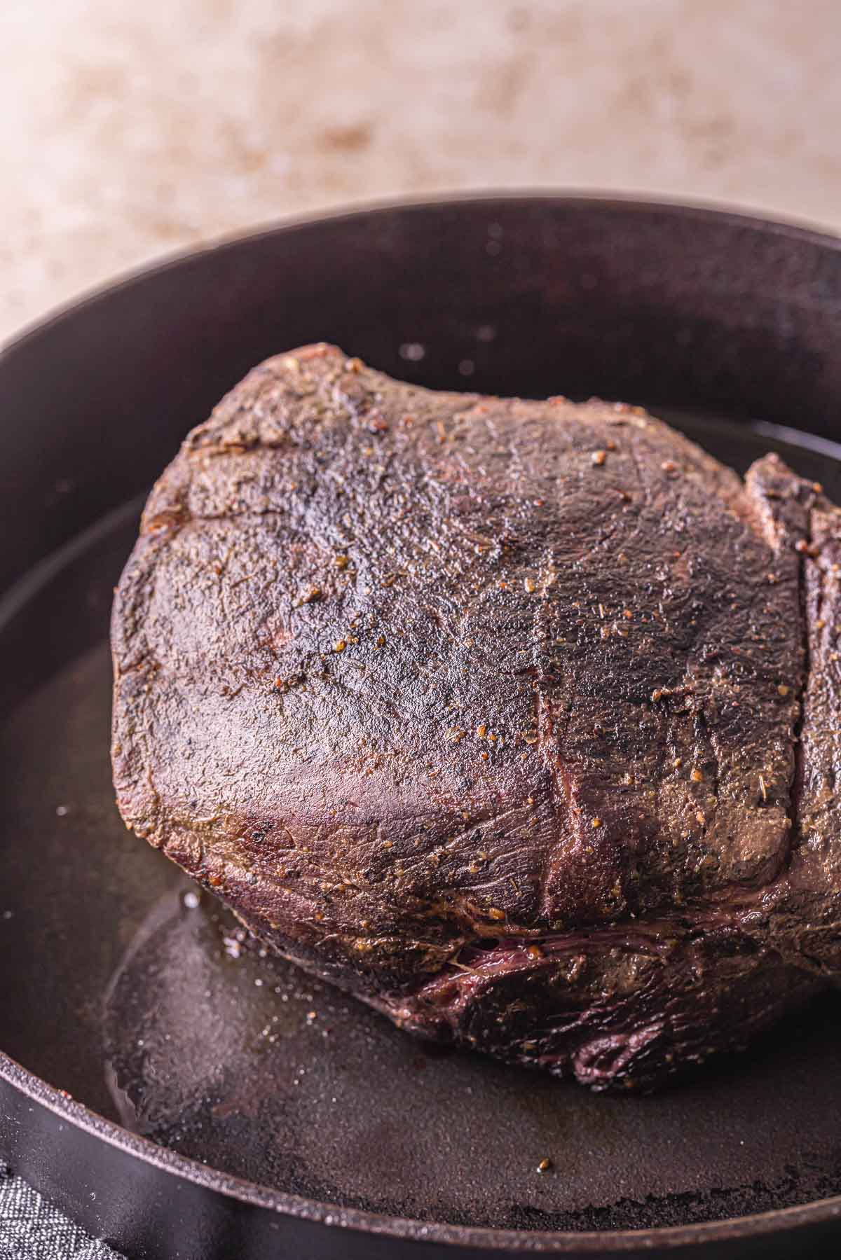 a beef roast being seared in a skillet