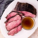 a sliced beef roast on a plate with a bowl of jus