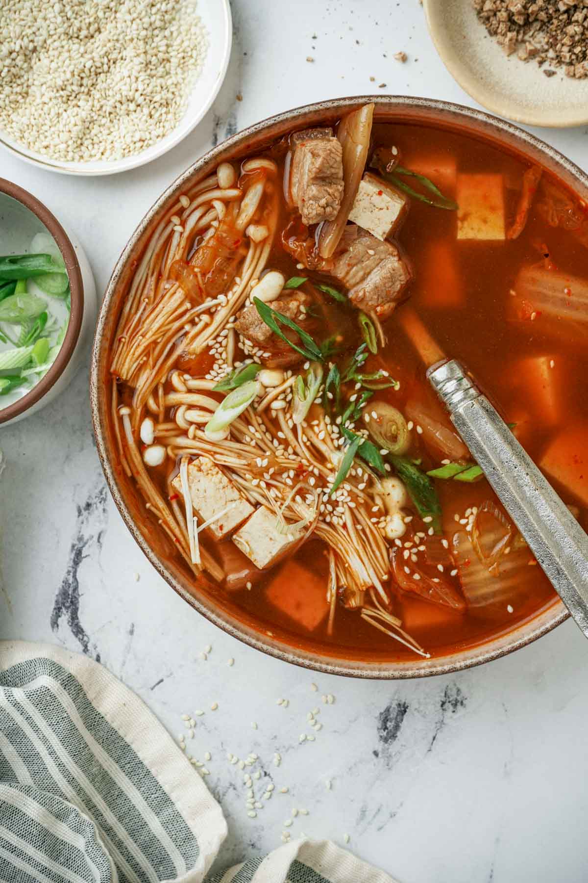 a spoon in a bowl of kimchi soup with tofu and onions