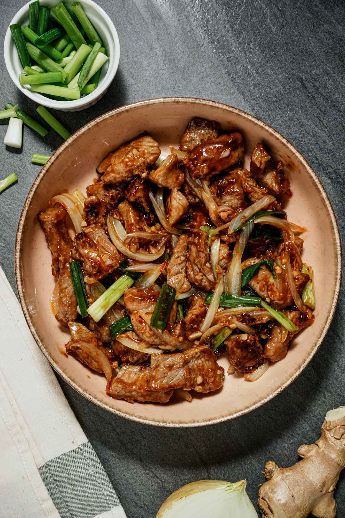a bowl of stir fried meat and onions with green onions