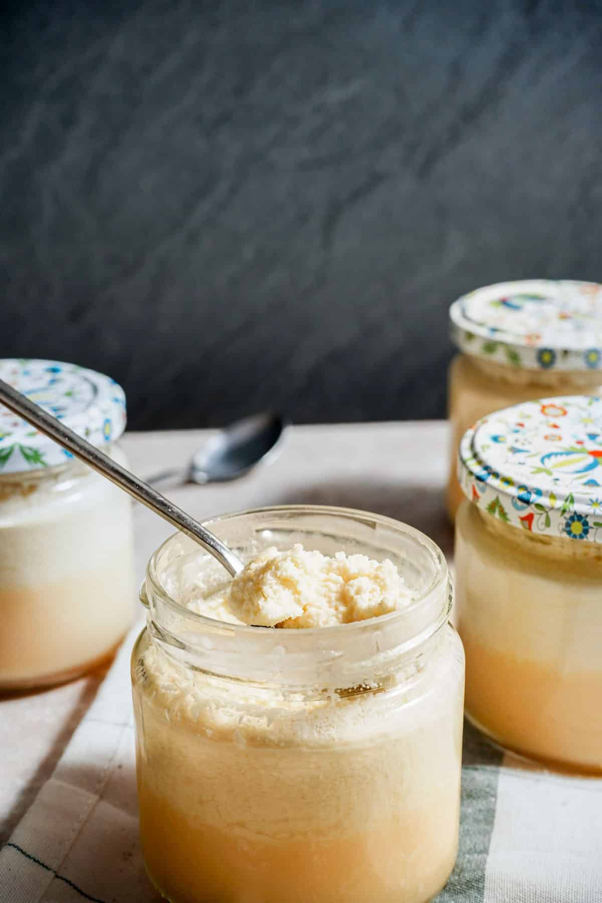 a spoon in a jar of custard with other jars surrounding it