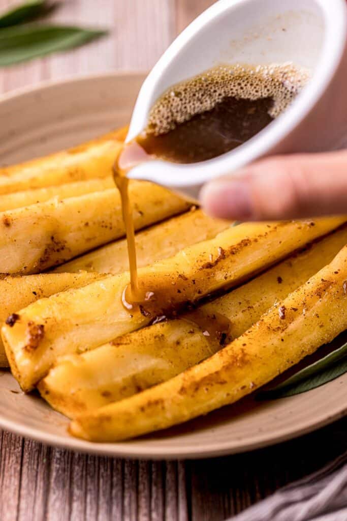 brown sauce being poured over a plate of cooked parsnips