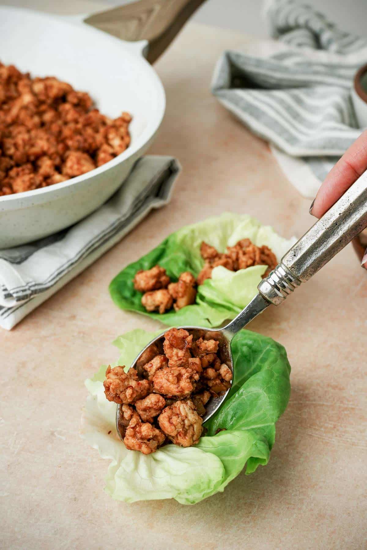 spooning red ground chicken mixture into a lettuce cup