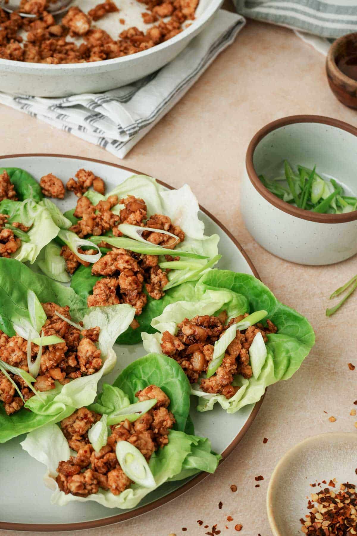 a plate of szechuan chili chicken lettuce wraps with green onion on the side