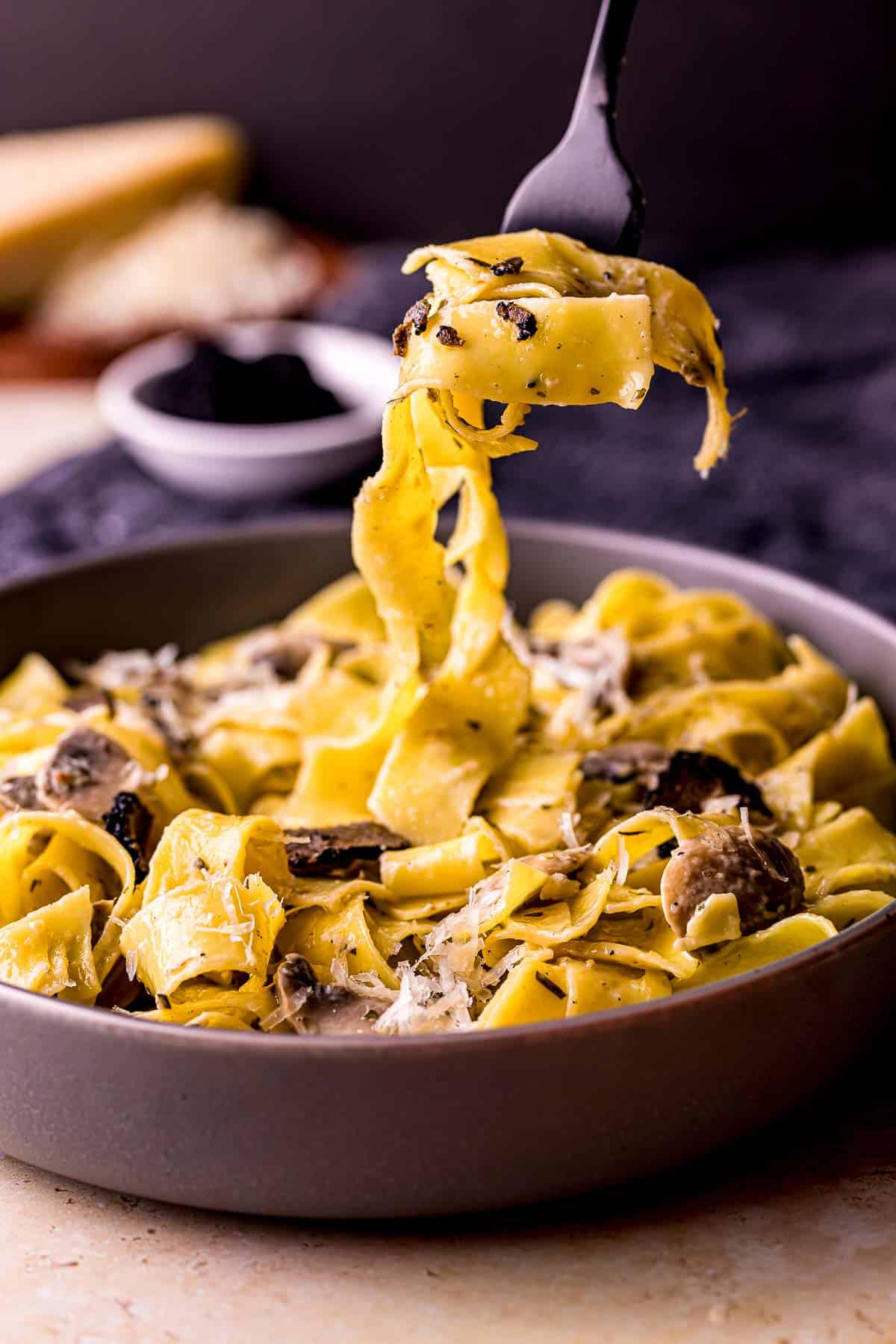a fork holding pasta over a dish of creamy pasta covered with truffles