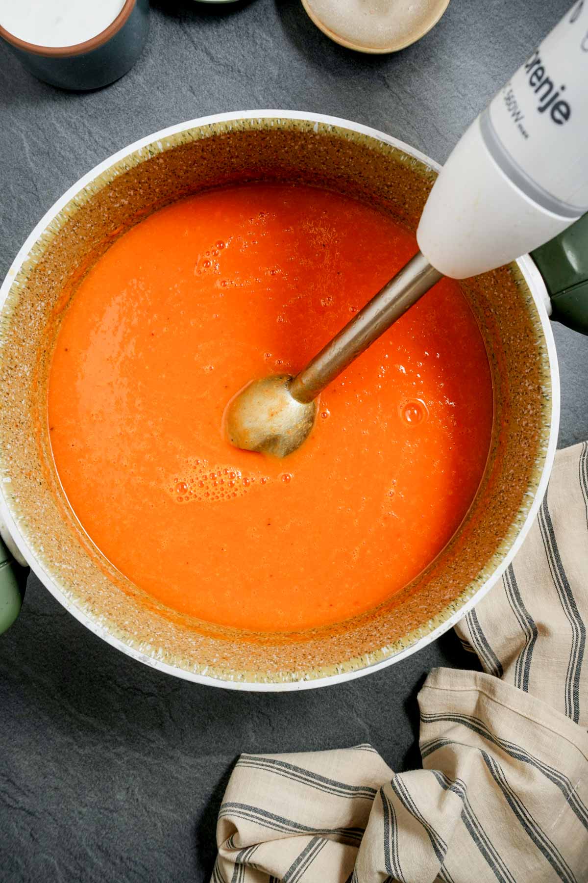 orange colored soup being blended in a pot with an immersion blender