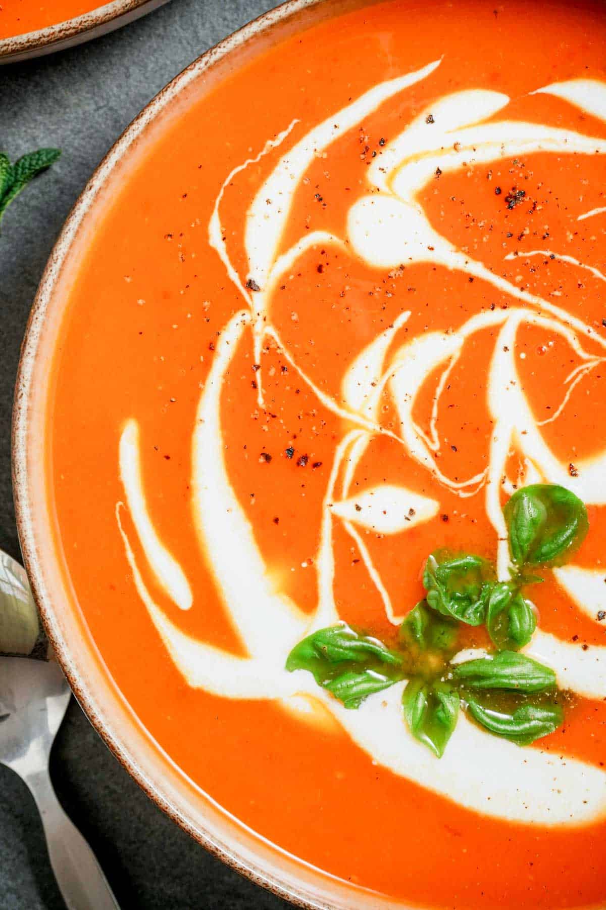 close up of a bowl of orange sweet potato soup with seasonings, herbs and cream swirled thorugh