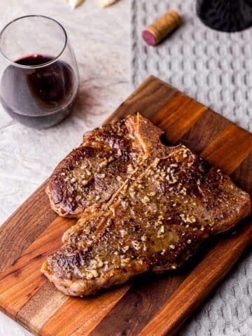a browned steak on a cutting board with a glass of wine