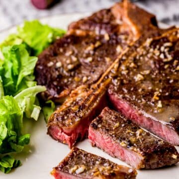 a steak served slice on a platter with greens on the side