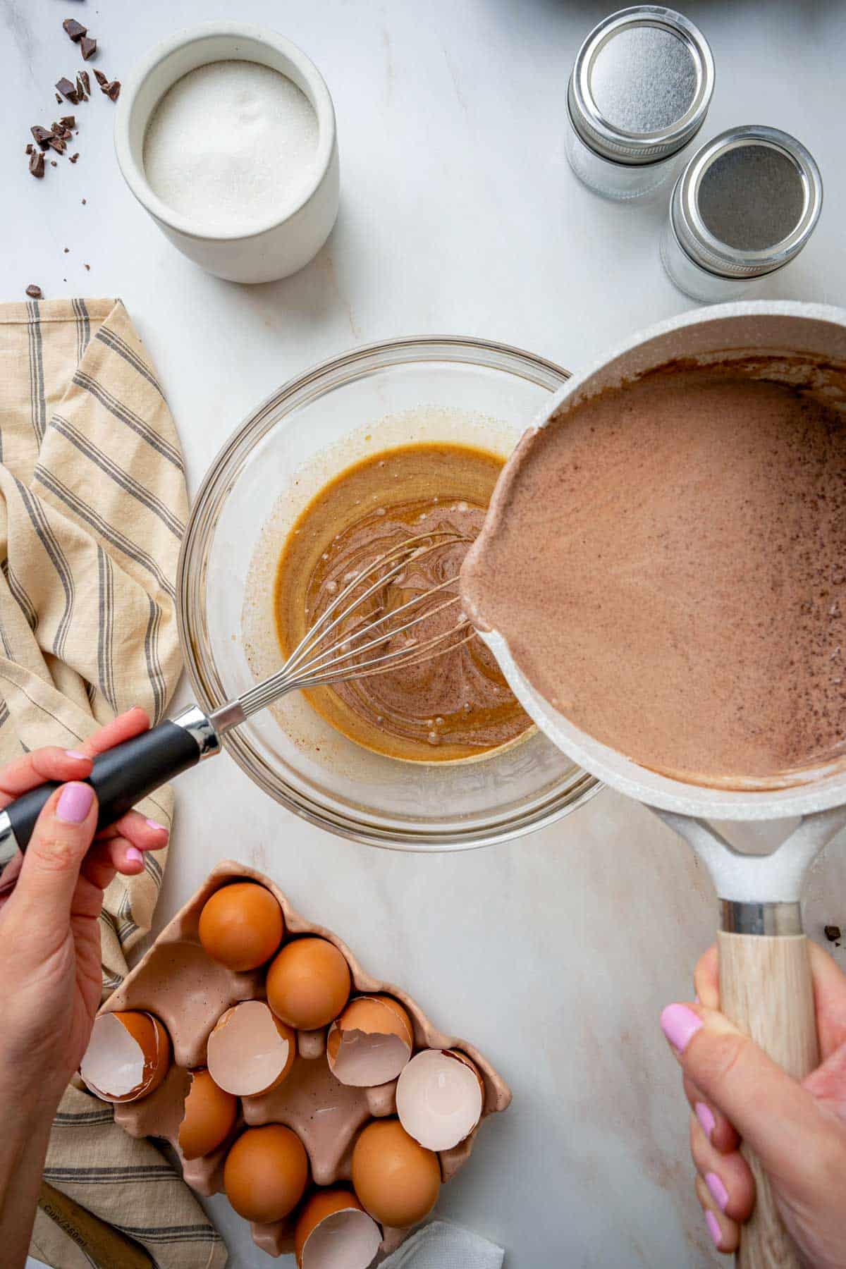 a brown chocolate mixture being poured into egg yolks while whisking