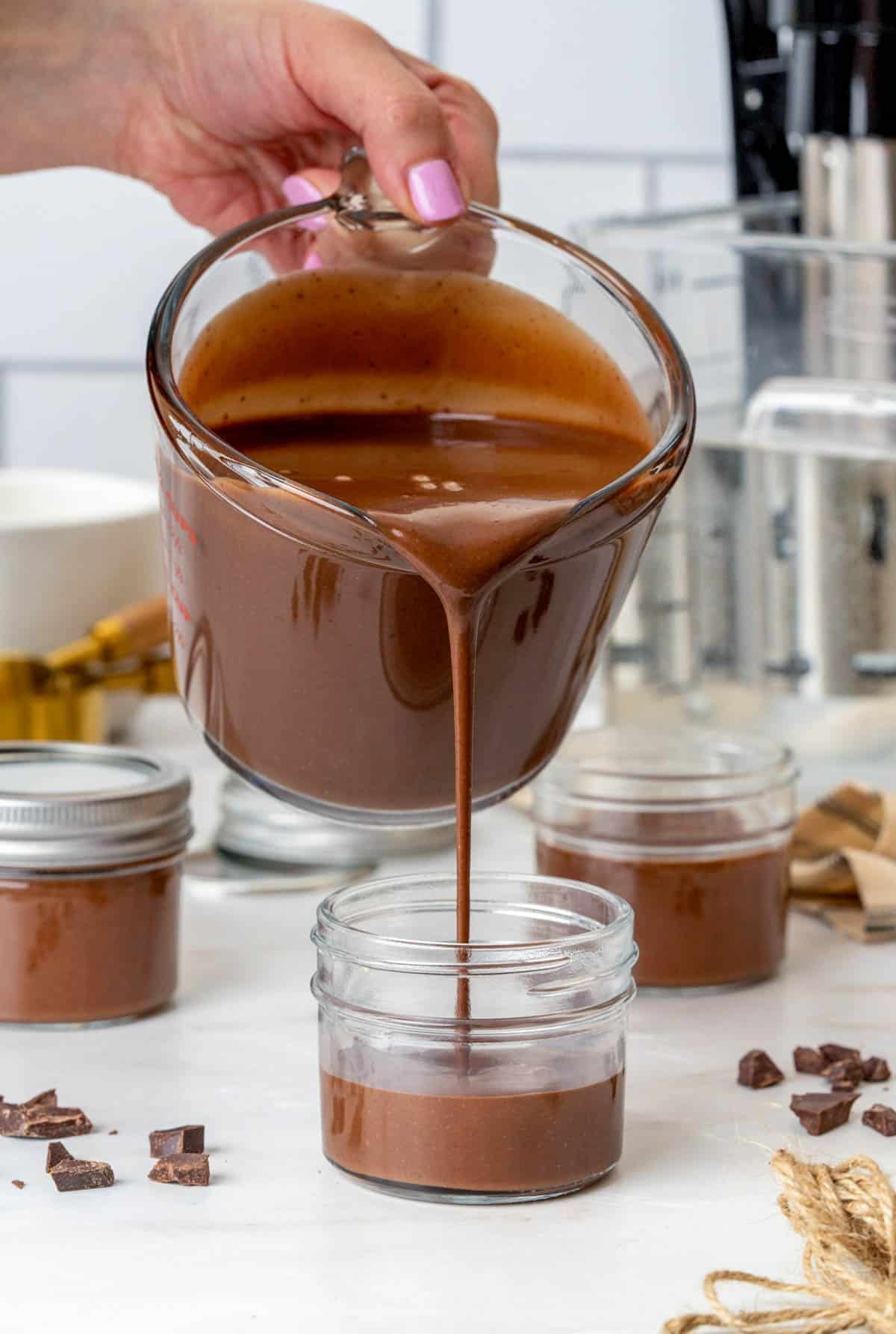 a measuring cup pouring brown chocolate liquid in a jar