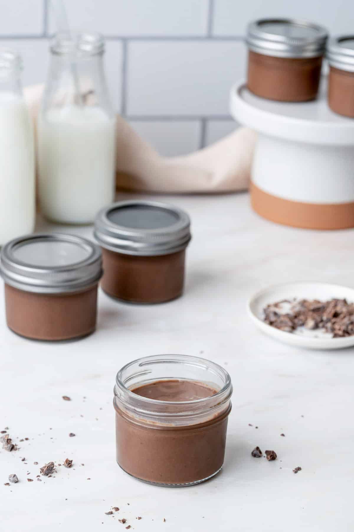 a jar of chocolate cream on a counter with other jars in the background