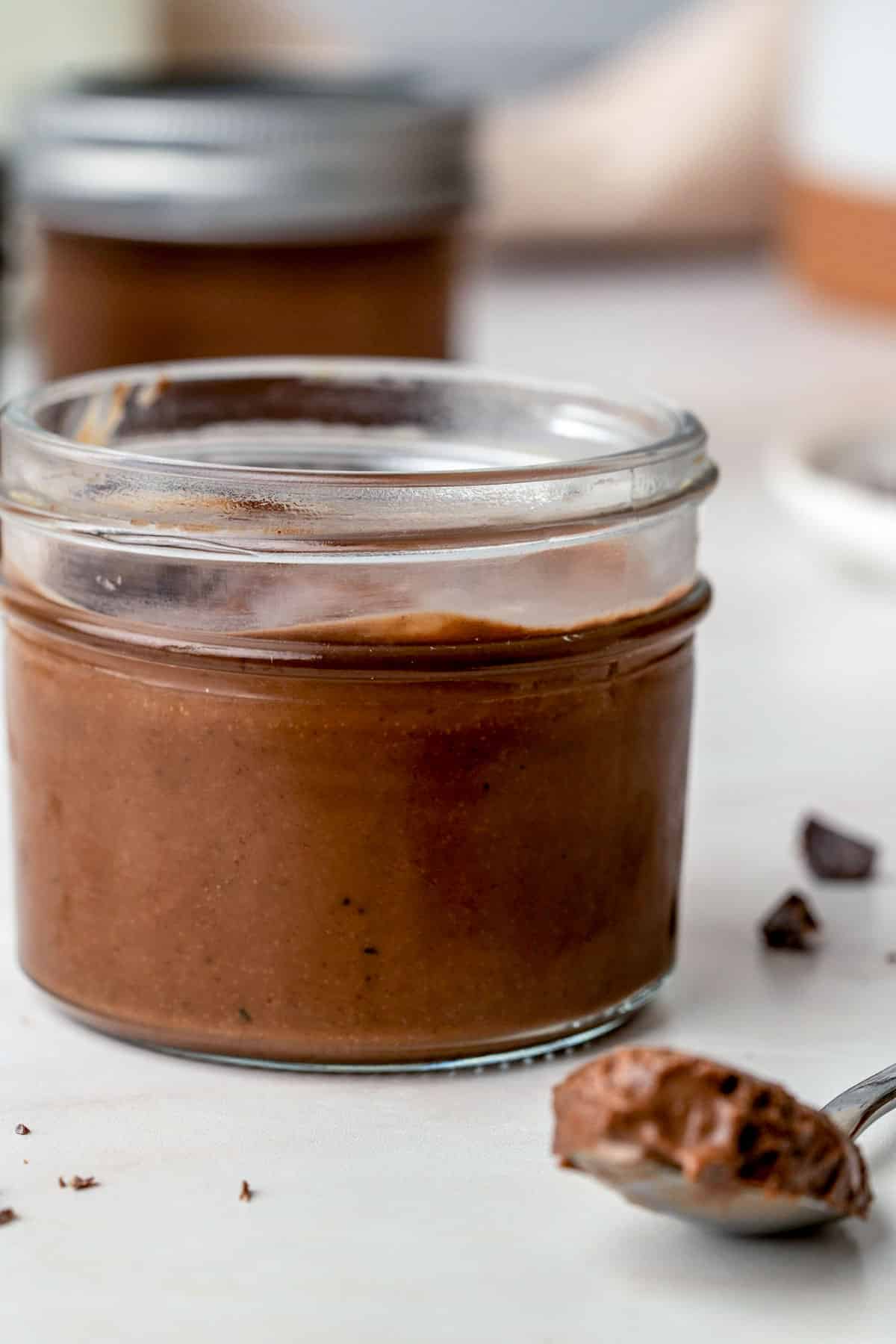 spoon of chocolate sitting next to a jar of chocolate dessert