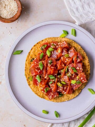 spicy tuna garnished with hot sauce, sesame seeds and green onions on a tostada