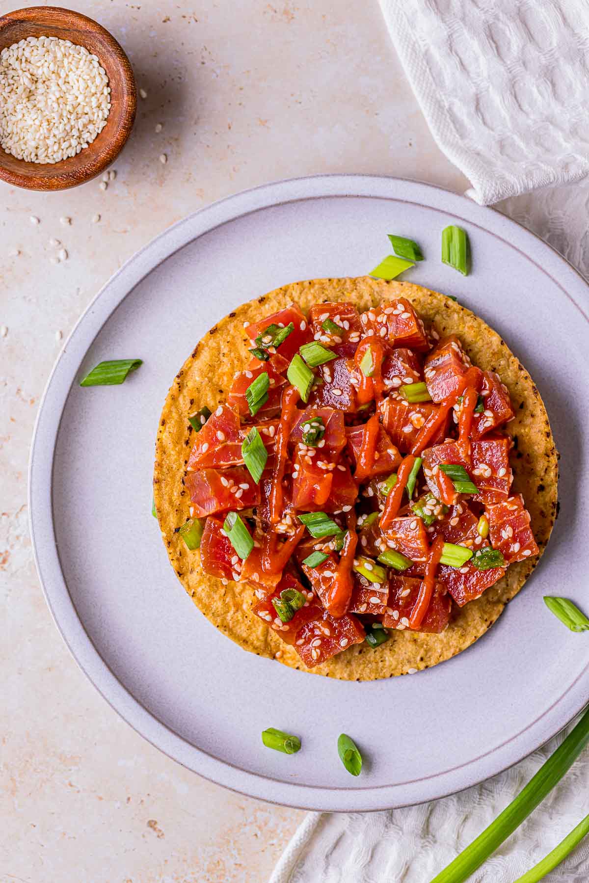 spicy tuna garnished with hot sauce, sesame seeds and green onions on a tostada