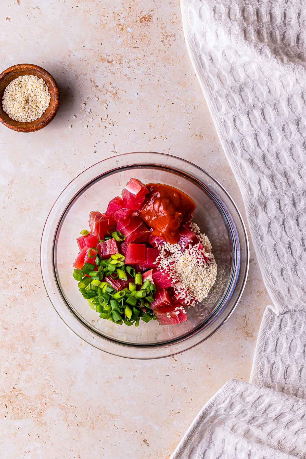 a glass bowl with chopped raw tuna, green onions, hot sauce and sesame seeds
