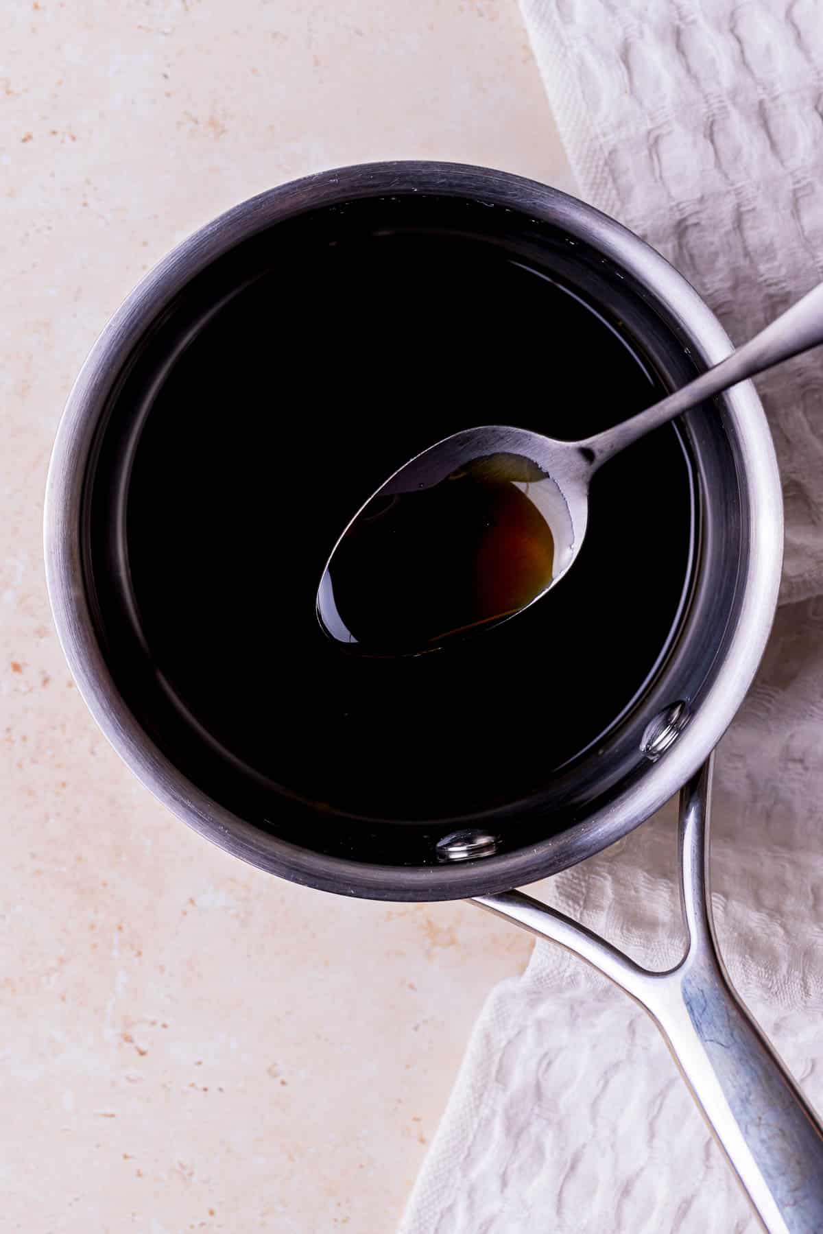 a spoon of dark sauce over top of a saucepan