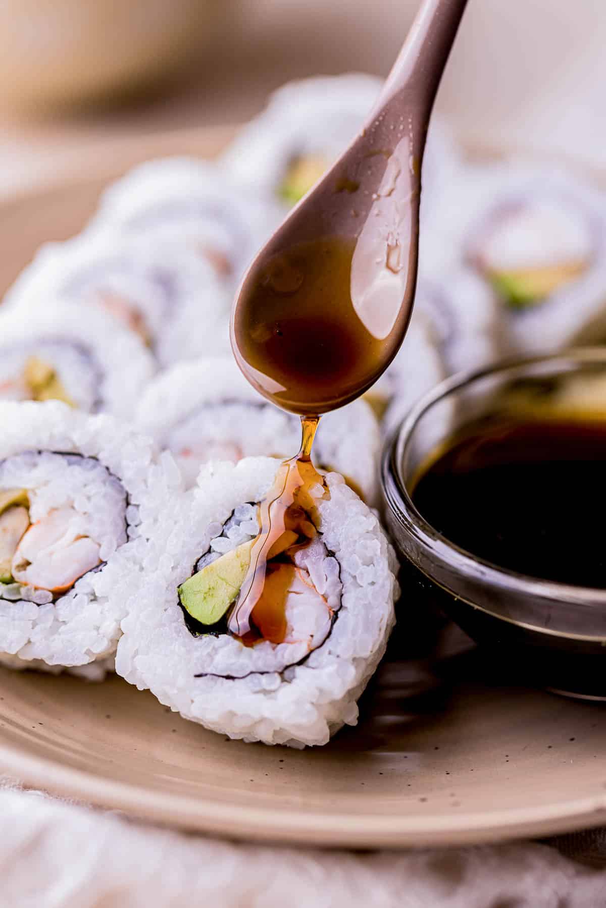 dark brown eel sauce being poured on a sushi roll