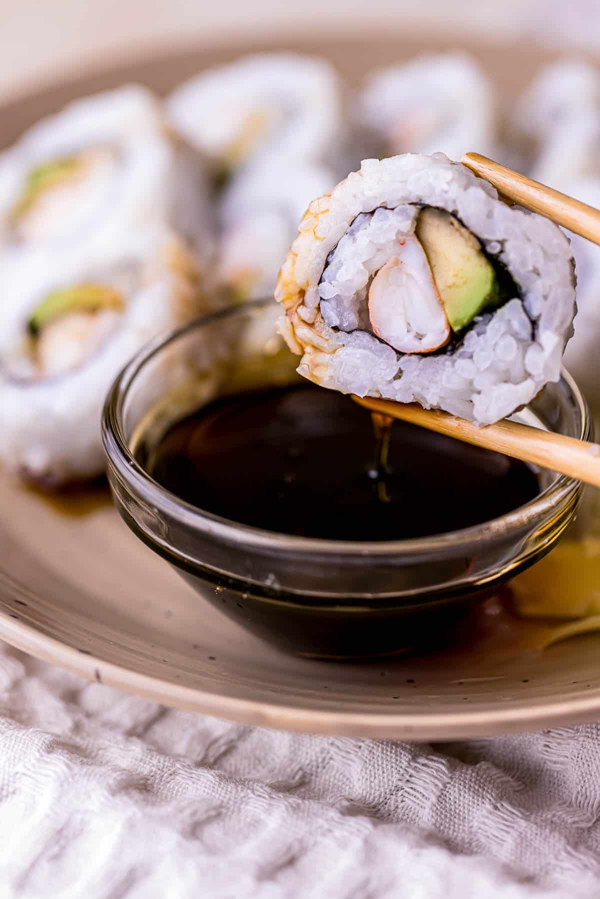 sushi being held by chopsticks and dipped in dark brown eel sauce