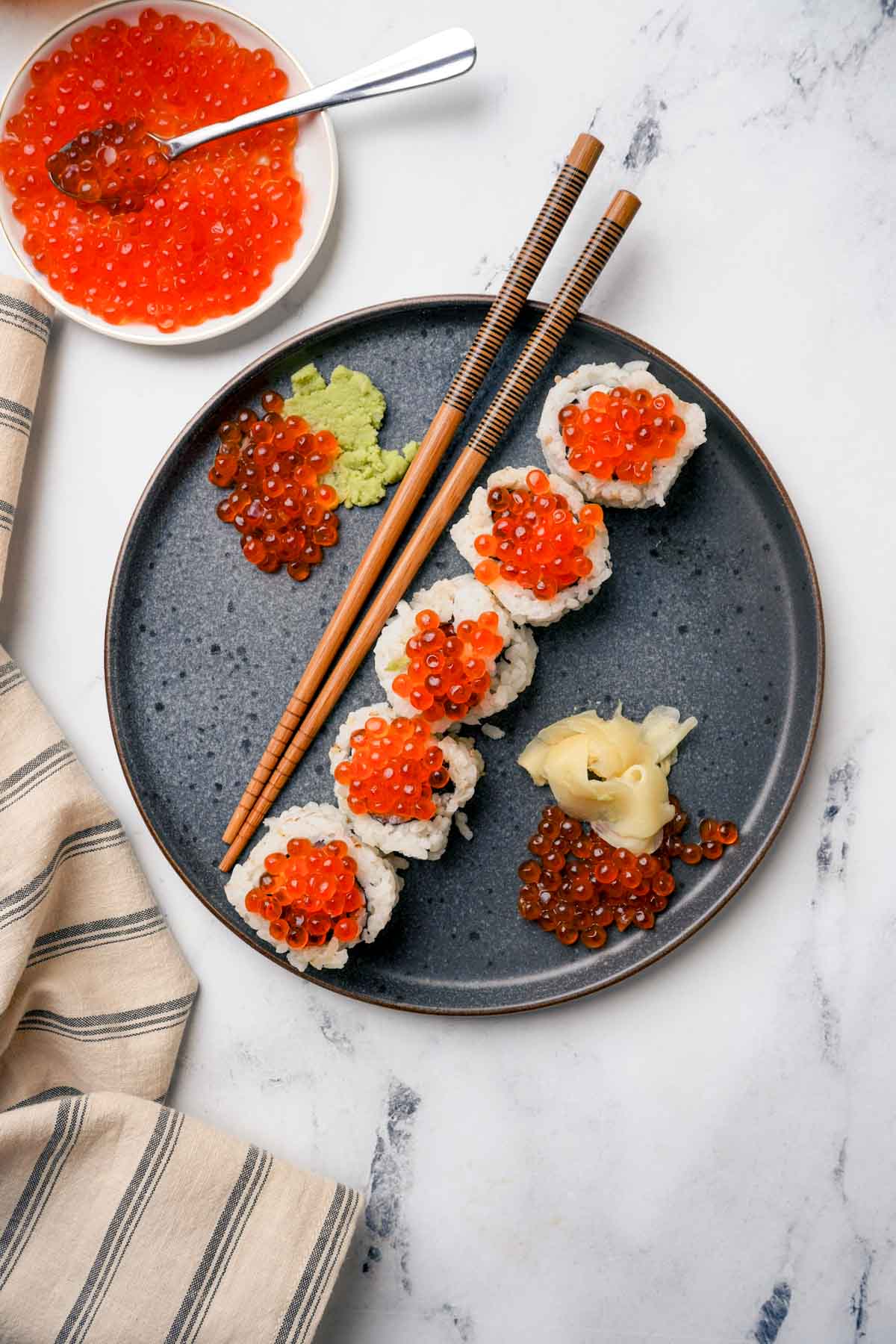 a plate of salmon caviar (ikura) sushi rolls with chopsticks
