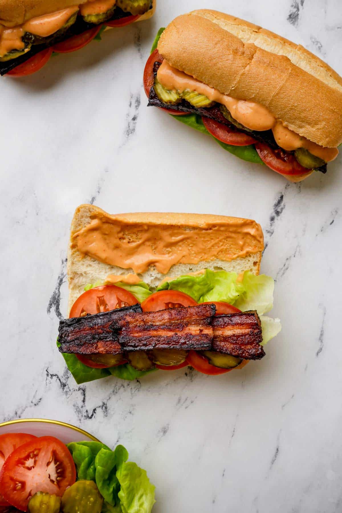 building a sandwich with lettuce, tomato and topped with roasted pork belly