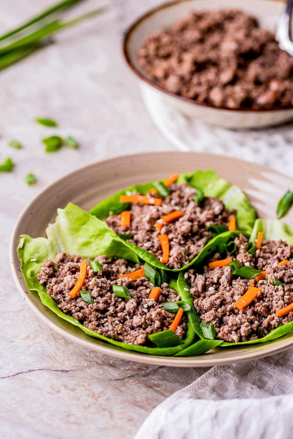 a plate of ground beef lettuce cups with carrots and green onions