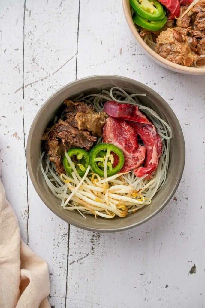 bean sprouts, shredded beef, rare beef, rice noodles and jalapenos in a bowl for pho tai
