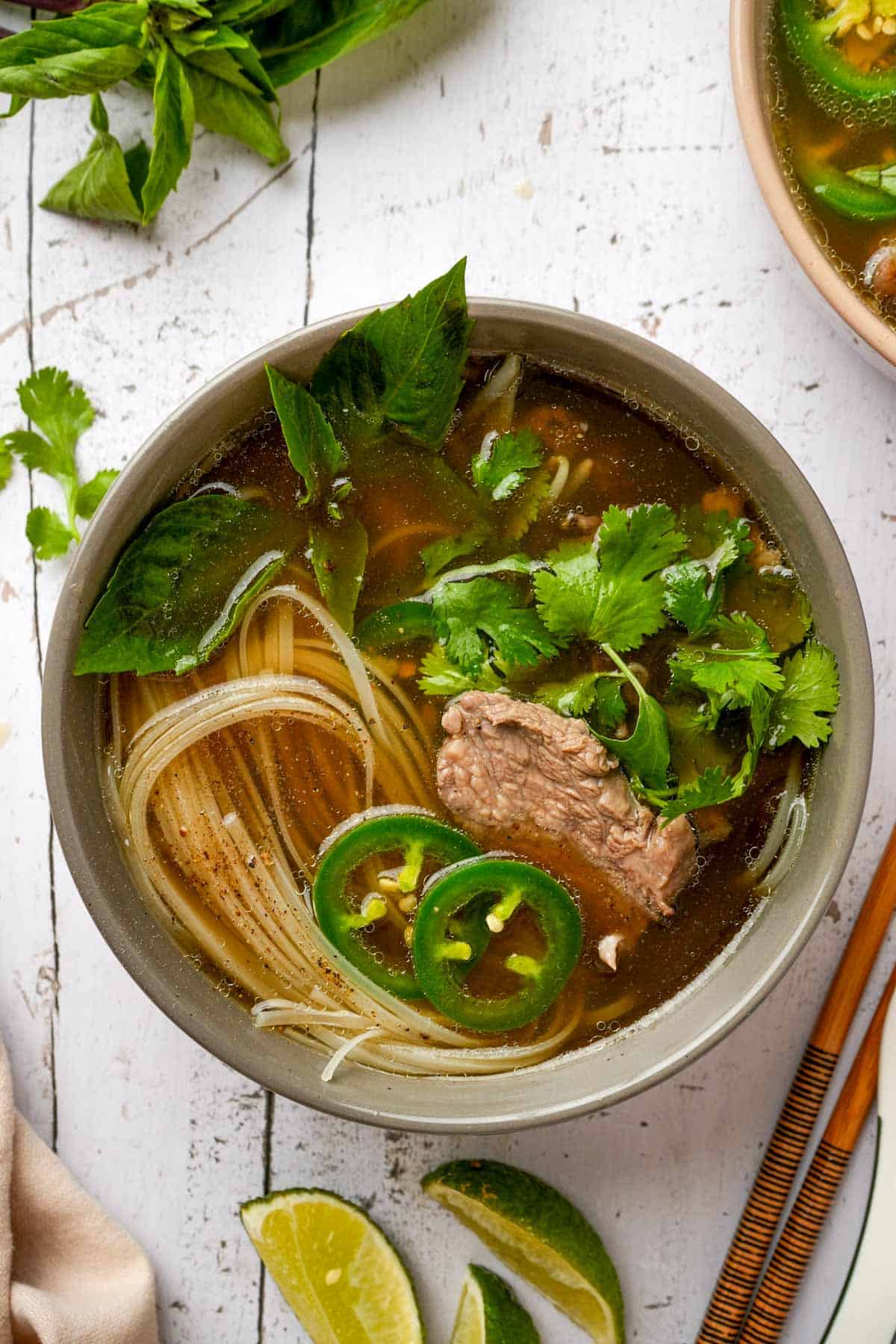 a bowl of Vietnamese beef pho with rice noodles and green herbs