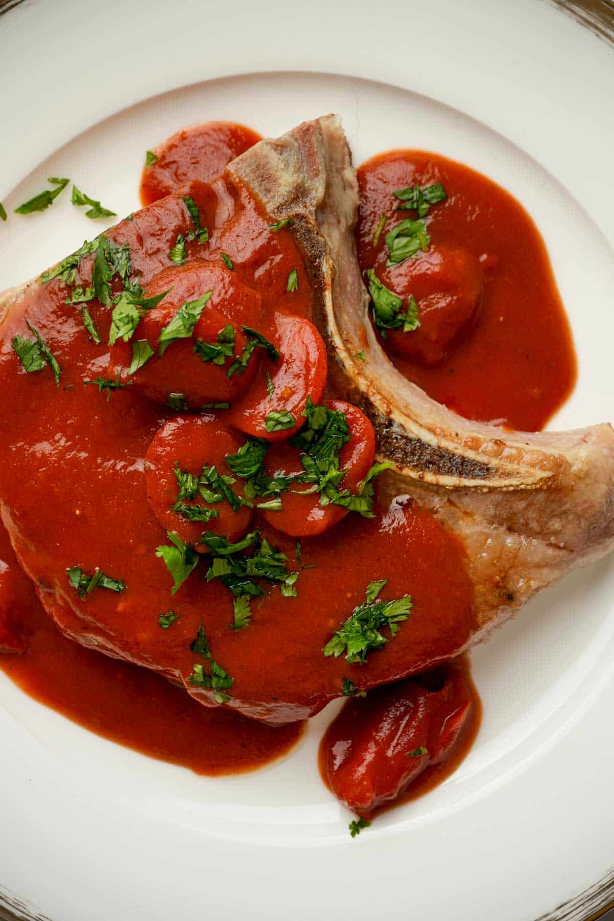 a sous vide pork chop with red tomato sauce and herbs on top