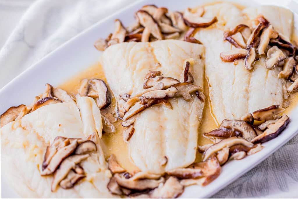 fish filets on a serving platter with mushrooms on top.
