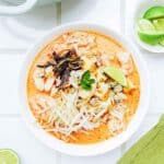 a bowl of laksa with noodles, seafood and limes.