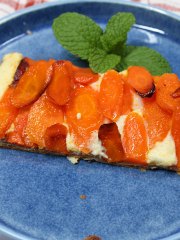 A rectangular slice of carrot tart with overlapping roasted carrot rounds and a sprig of fresh mint on a blue plate.