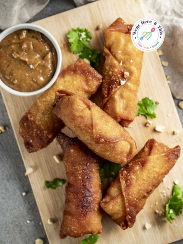 Crispy chicken pad thai egg rolls served on a wooden board with peanut dipping sauce.