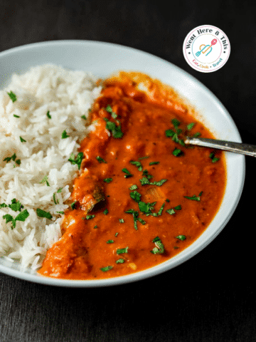 A white bowl of creamy Tomato Curry garnished with fresh cilantro, served with a side of fluffy white rice.