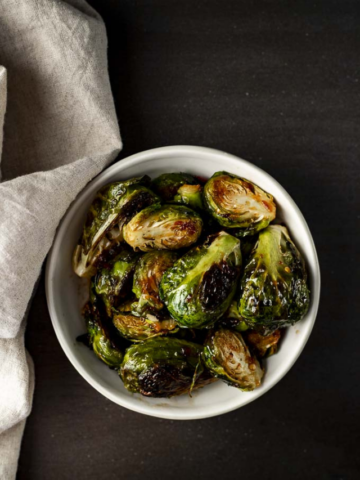 A white bowl filled with halved, oven-roasted Brussels sprouts showing deep caramelization and crispy, charred edges.