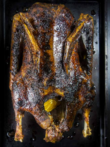 A whole roasted goose with dark, crispy skin and a honey orange glaze, presented on a dark baking sheet