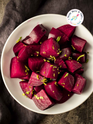 Close-up of vibrant, tender Instant Pot beets cut into wedges and garnished with fresh herbs in a white bowl.