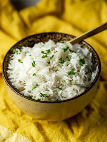 A bowl of fluffy cooked Basmati rice garnished with fresh parsley on a yellow napkin.