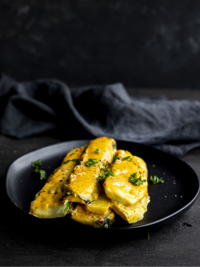Pan-seared white fish fillets drizzled with a creamy lemon butter sauce and garnished with fresh parsley on a black plate.