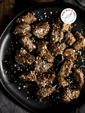Juicy air fryer steak tips seasoned with herbs and topped with blue cheese crumbles on a black plate.